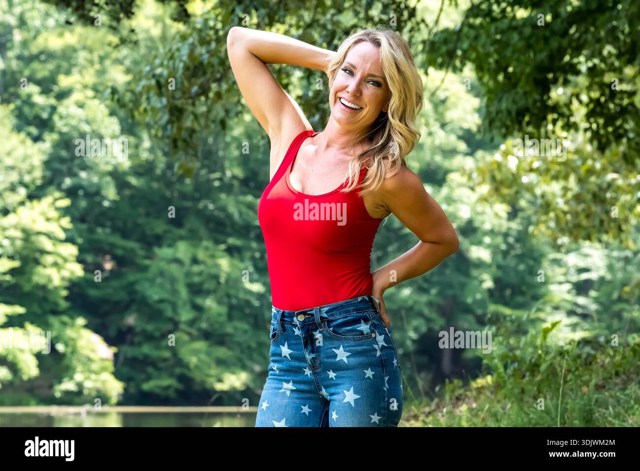Eine schöne blonde Frau in Americana-Kleidung entspannt sich am Unabhängigkeitstag am See, saugt die Sonne und den festlichen Geist auf, verkörpert Freiheit, Freude, A Stockfoto