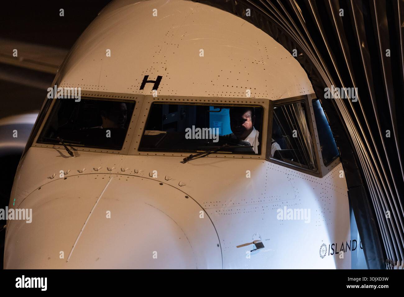 Cockpit-Blick auf einen kommerziellen Jet am Gate, wobei Piloten bei der Vorbereitung vor dem Flug nachts durch die Windschutzscheibe sichtbar sind. Stockfoto
