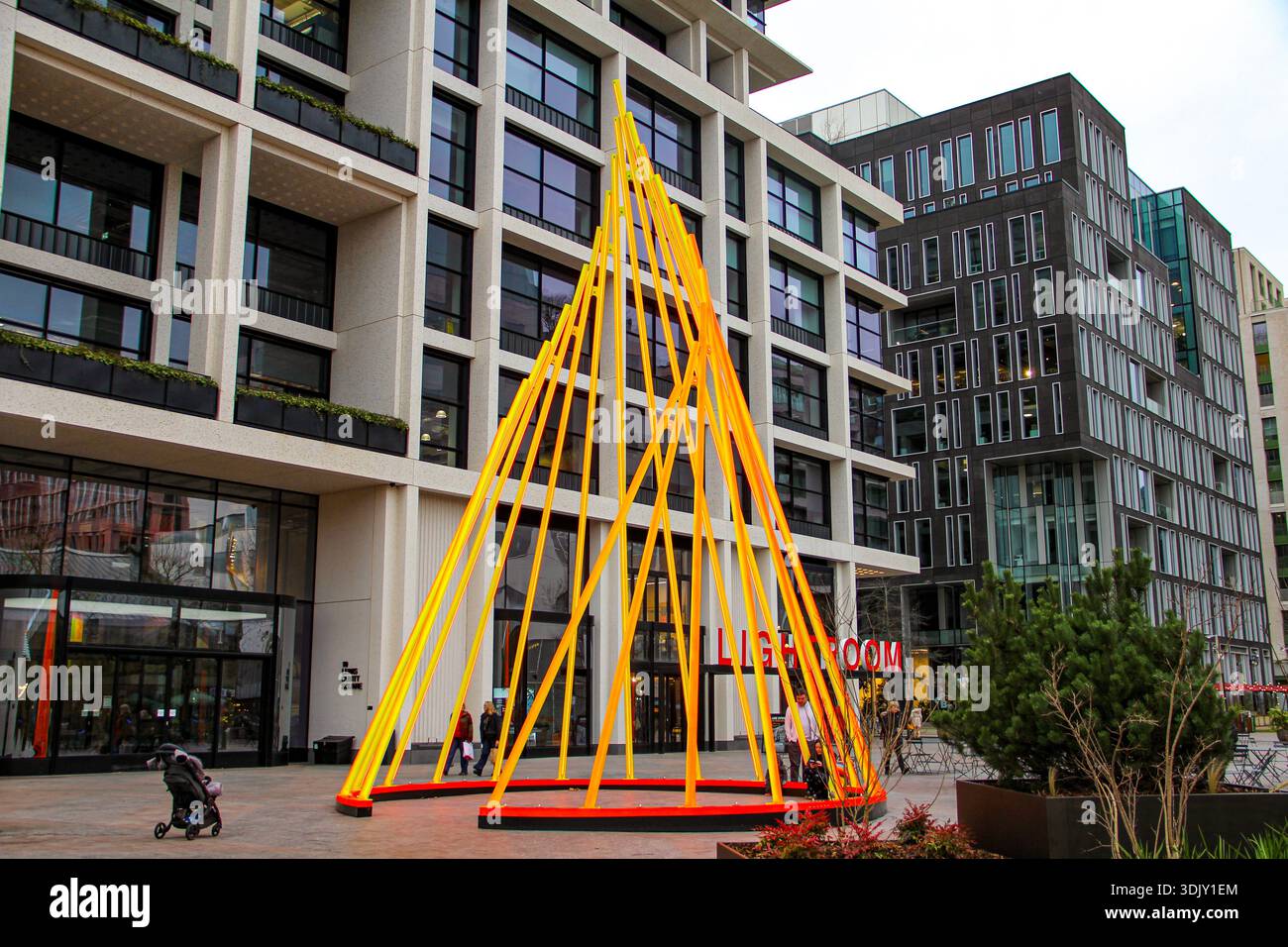 Zeitgenössische gelbe, kegelförmige geometrische Skulptur, die auf einem modernen, städtischen plaza, umgeben von kontrastreichen hellen und dunklen Stadtgebäuden, installiert ist. Stockfoto