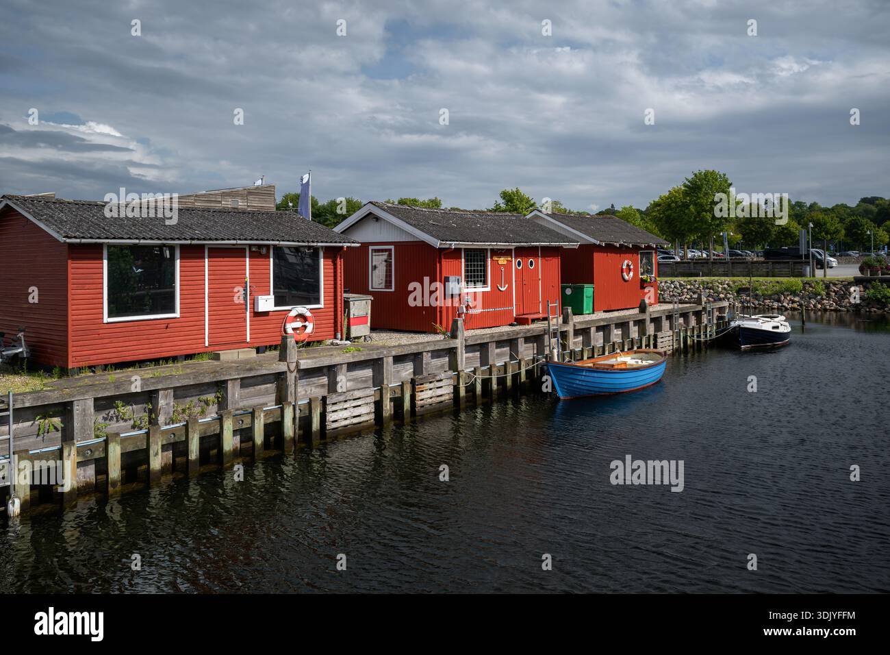 Ein kleines Boot ruht neben roten Holzhäusern im Hafen von Roskilde. Stockfoto