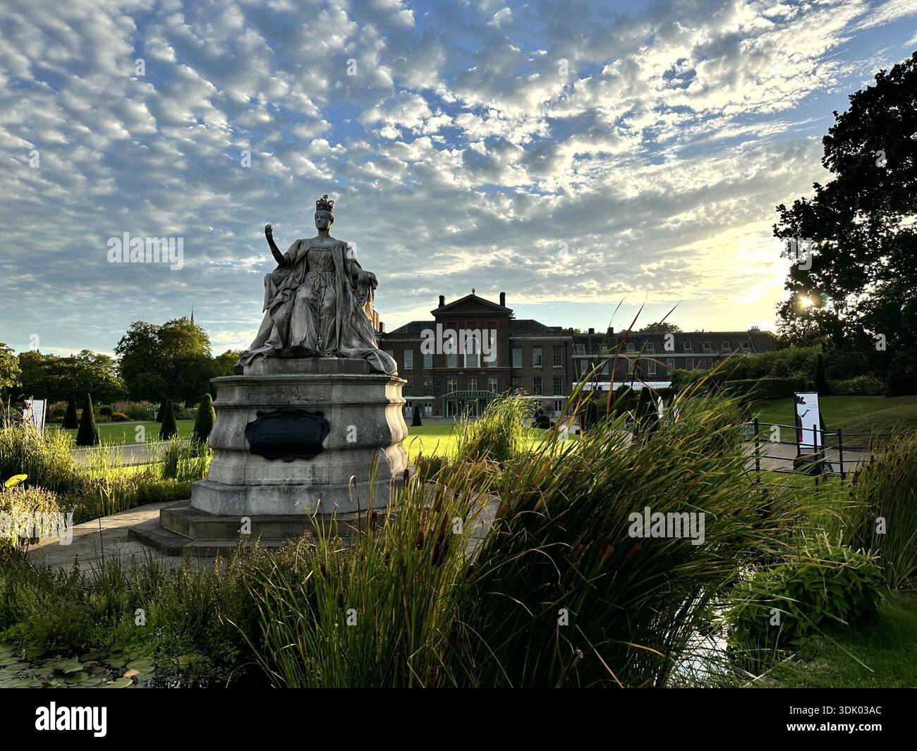 Statue in den Kensington Gardens in der Nähe des Kensington Palace, London, mit historischer Architektur, Landschaftsgärten und dramatischen Abendwolken. Stockfoto