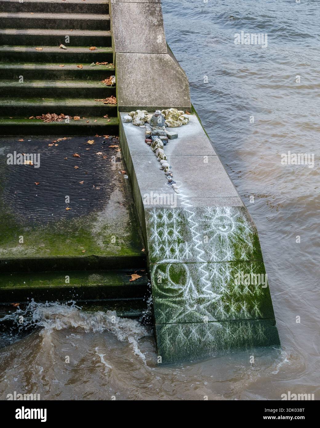 Kreidezeichnungen und angeordnete Steine auf abgenutzten Steintreppen am Rand der Themse, die Gezeitenwasser und Algenwachstum zeigen. Stockfoto