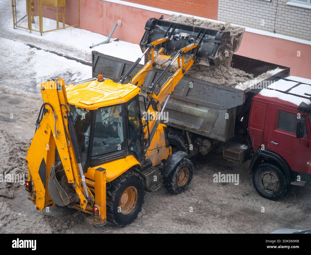 Schneeräumungs-Traktor, der schmutzigen Schnee in den Müllwagen im Stadthof lädt, Konzept der saisonalen Reinigung, Stadtverkehr. Stockfoto