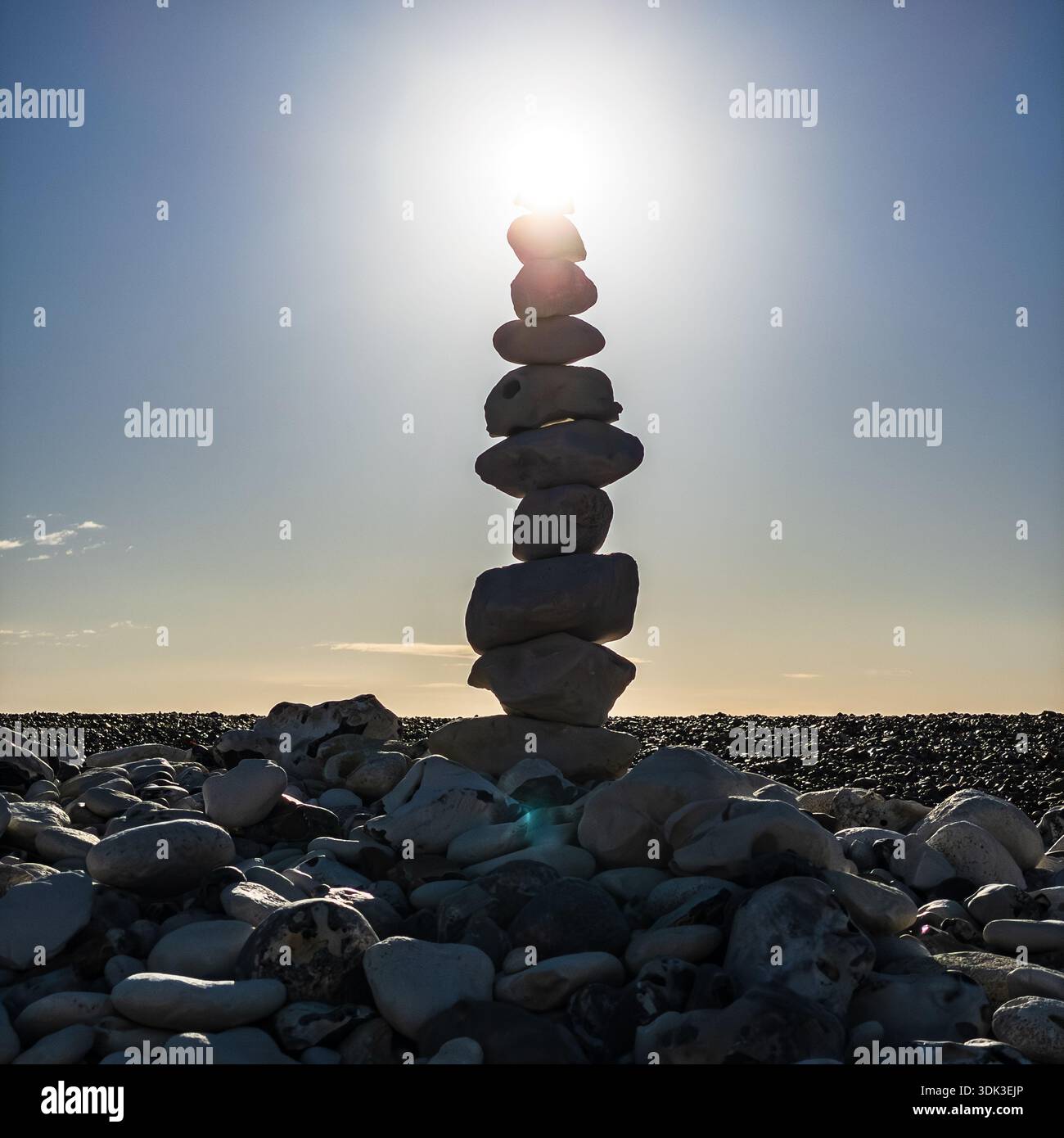 Ein ausgewogener Kirchturm aus Kieselstein, der bei Sonnenuntergang gegen intensive Sonnenstrahlen an einem Kieselstrand gehalten wird, symbolisiert Harmonie und Ruhe - Smartphone-aufgenommenes Stockfoto