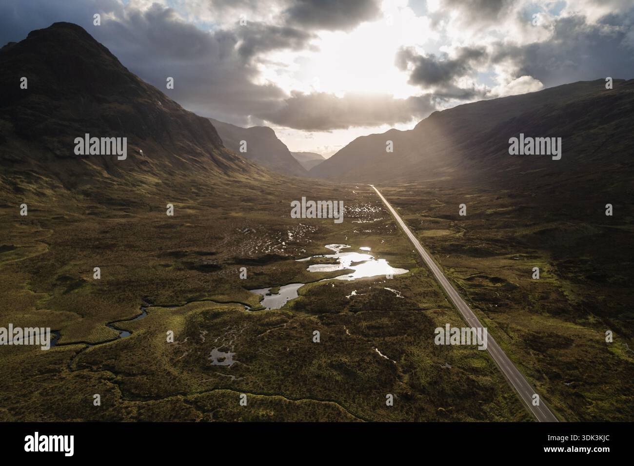 Aus der Vogelperspektive führt ein Straßenband durch das dramatische, schattige Tal von Glen Coe, unter einem Himmel, durchbohrt von strahlendem Sonnenlicht, Glen Coe, Schottland, U Stockfoto