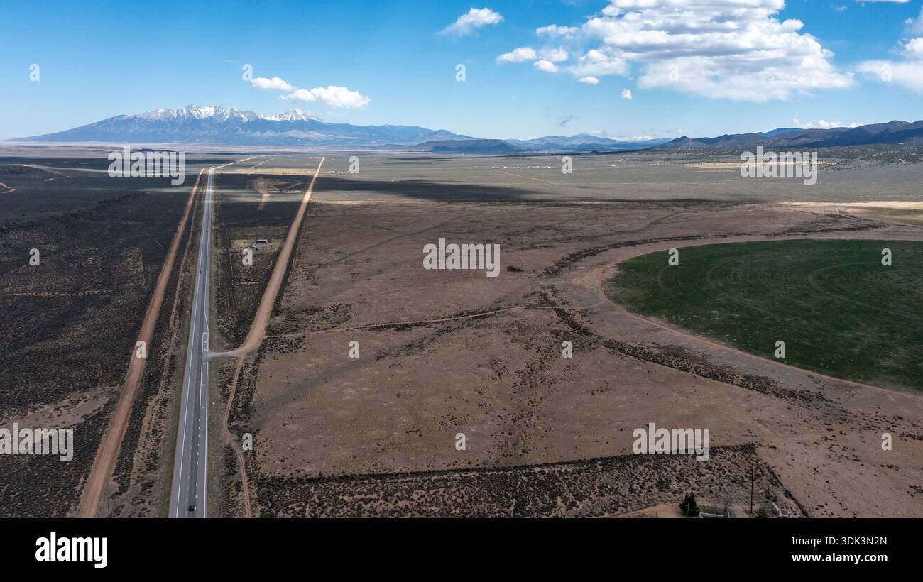 Blick auf ein langes Autobahnband, das sich über die trockene Landschaft in Richtung entfernter schneebedeckter Berge unter einem riesigen blauen Himmel erstreckt, Winslow, Arizona, U Stockfoto