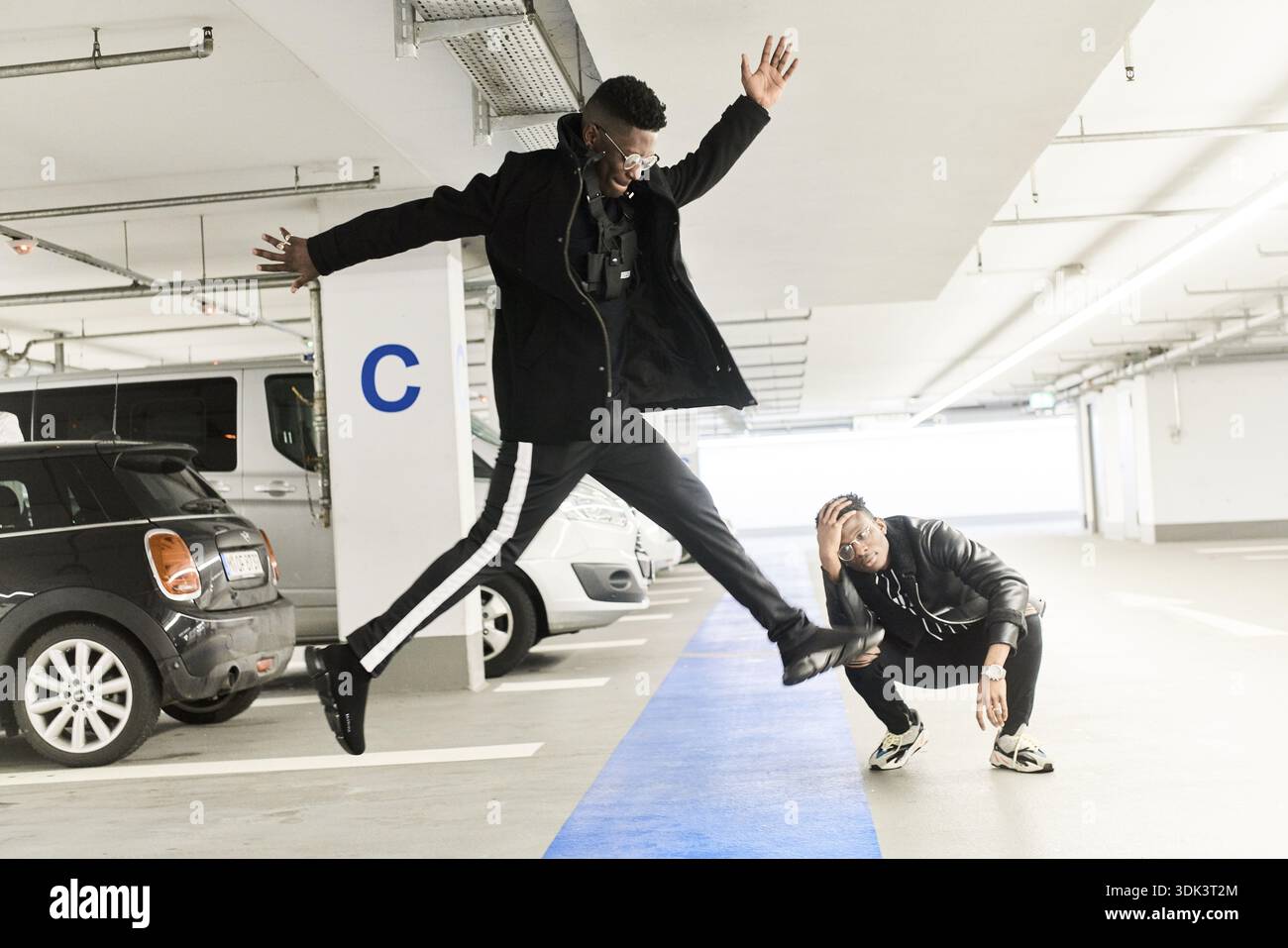 Beste Erstlinge, modisch, Coolness, Springen auf dem Parkplatz, zwei Freunde in einer Parkgarage, wobei einer spielerisch springt und eine dynamische, j Stockfoto