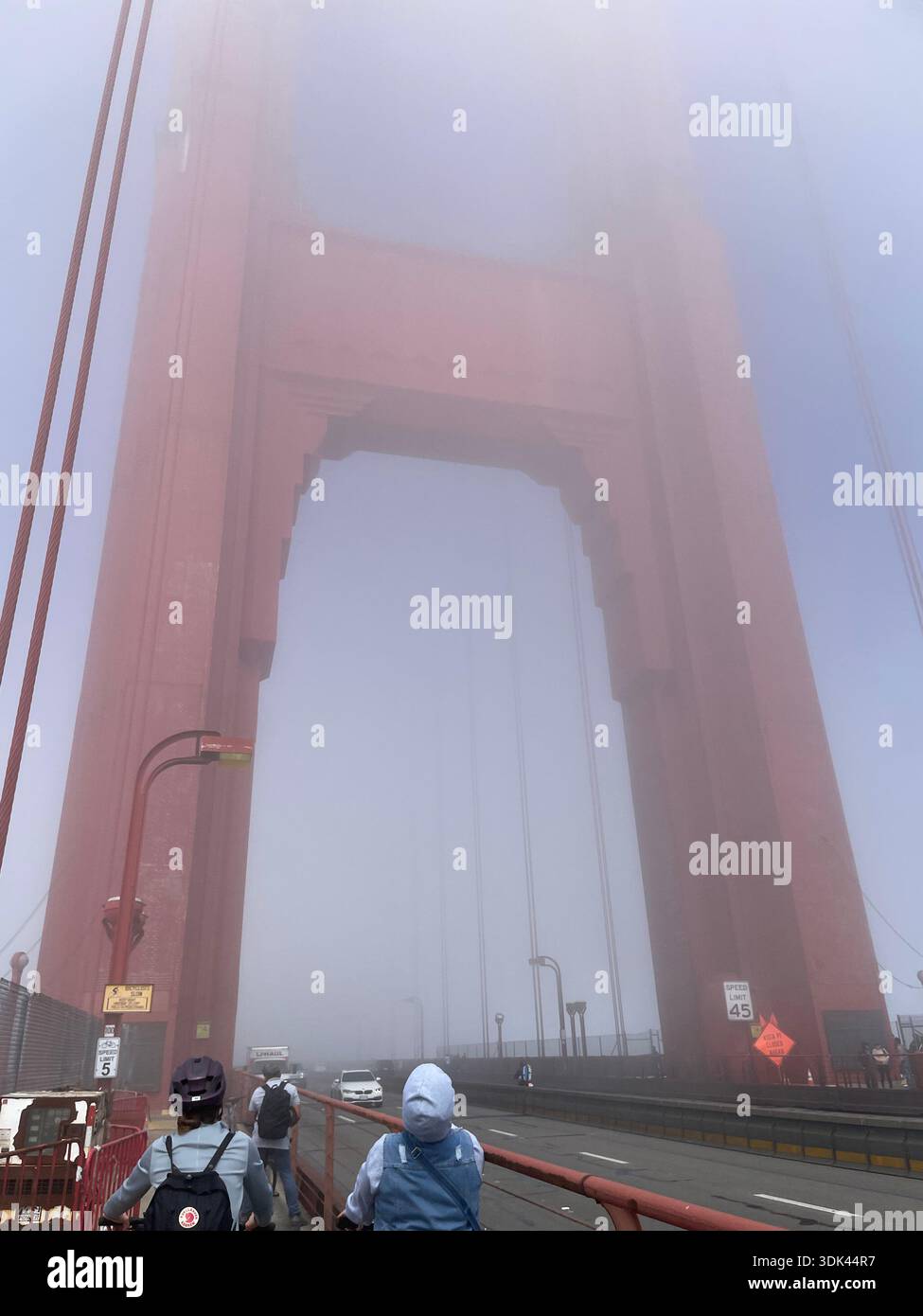 Der Golden Gate Bridge Tower ist in Nebel gehüllt und hat Fußgänger auf dem Fußweg, San Francisco, Kalifornien, USA. - Smartphone-aufgenommenes Stockfoto