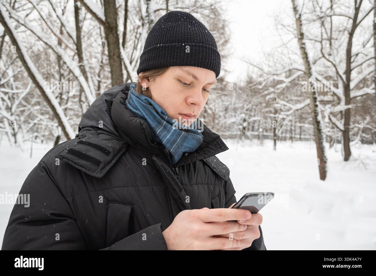 Junger Mann mit Smartphone im verschneiten Wald Stockfoto