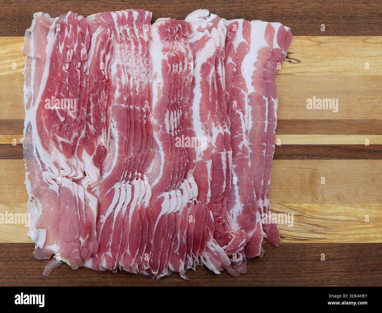 Geräucherte, dünn geschnittene ​​bacon mit sichtbarer Fettstruktur wird auf einem Holzbrett gestapelt. Draufsicht. Kopierraum. Stockfoto
