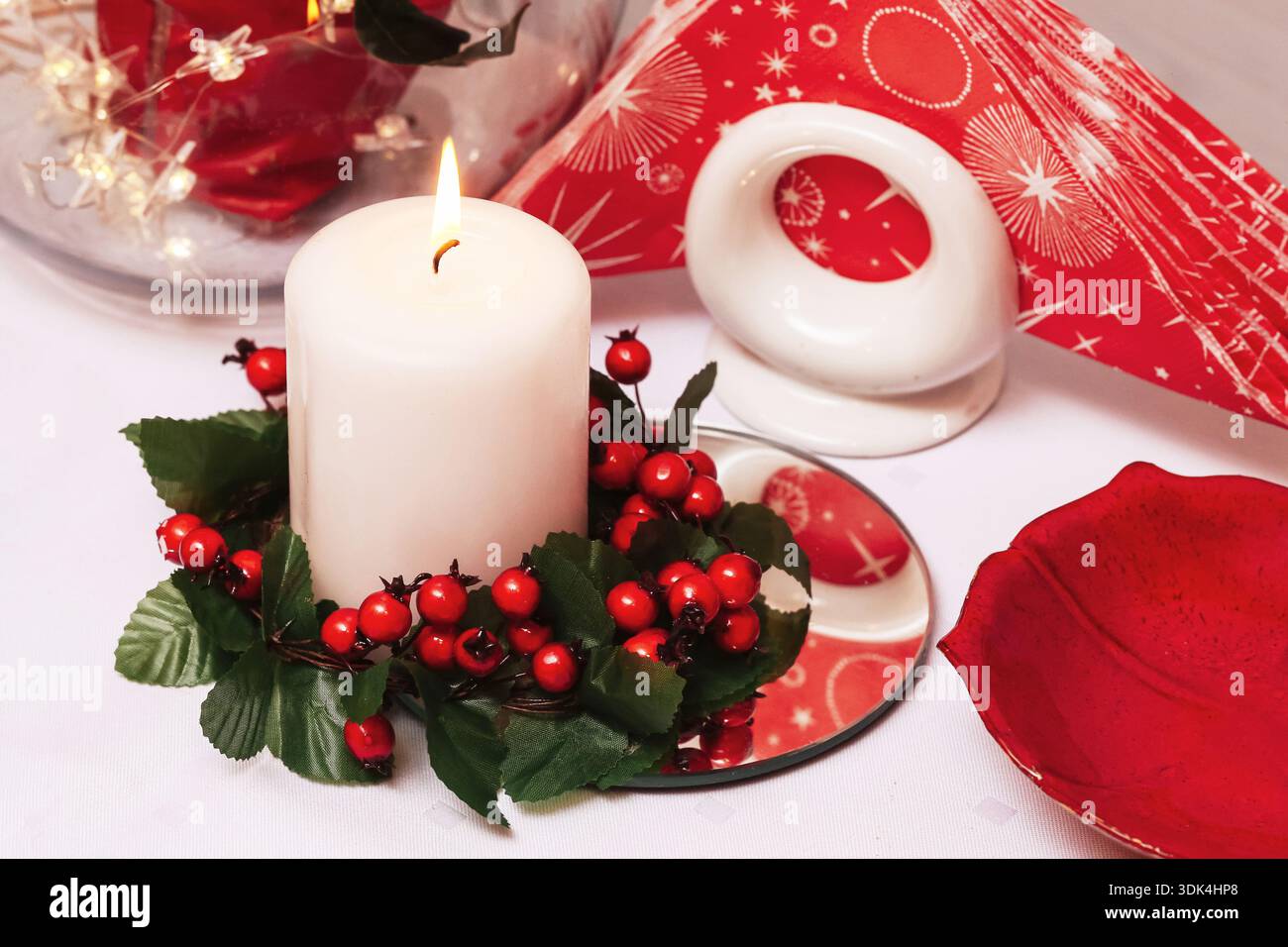Herzstück der Weihnachtskerze mit roter Dekoration. Adventsweihnachtstisch. Festliches Winterstilleben mit warmem Licht und saisonalen Ornamenten. Stockfoto