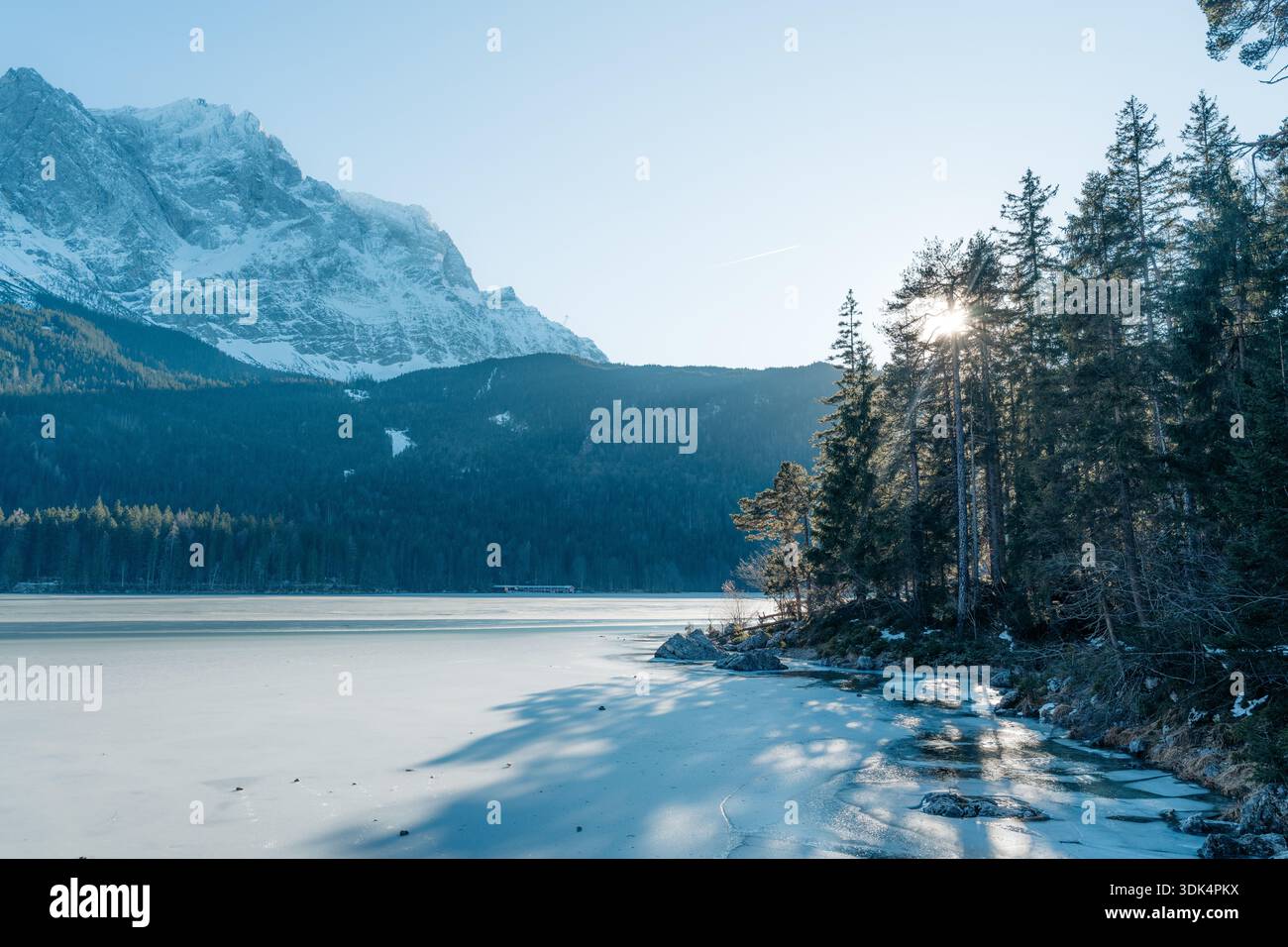Gefrorener Eibsee, Zugspitze und sonnendurchflutete Kiefern im bayerischen Winter. Idyllische Landschaft Stockfoto