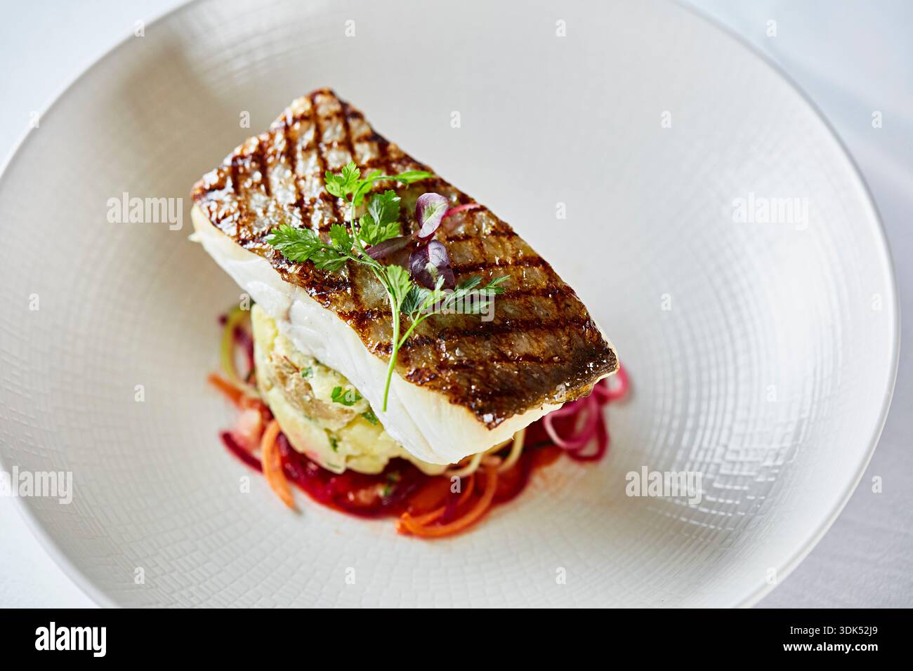 Gegrilltes Wolfsbarschfilet auf einem Bett aus Kartoffeln und Gemüse Stockfoto