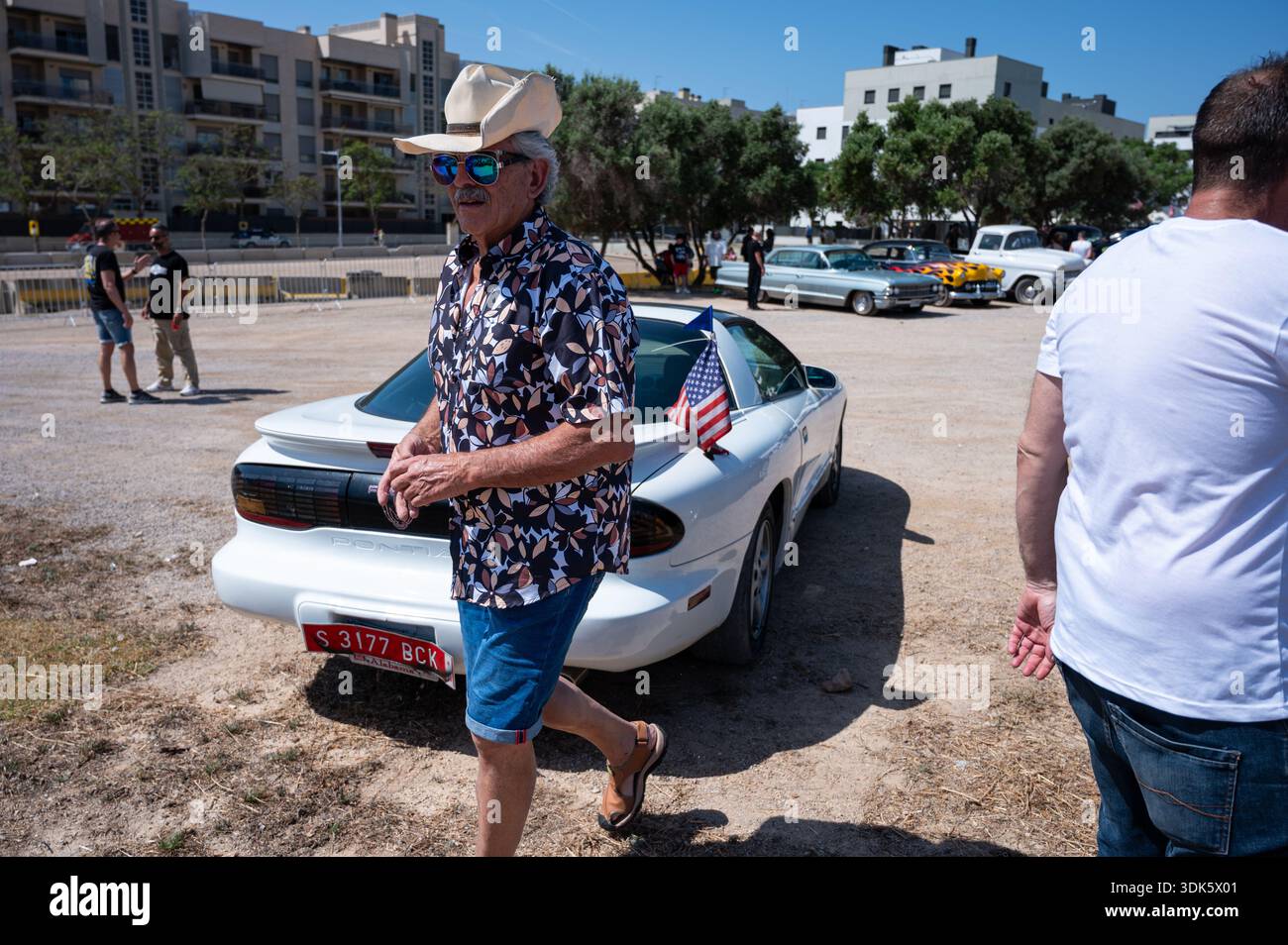 Rückansicht eines weißen Pontiac Firebird der vierten Generation, mit einem Mann mit Strohhut und Sonnenbrille, der auf einer Autoausstellung an ihm vorbeiläuft. Stockfoto