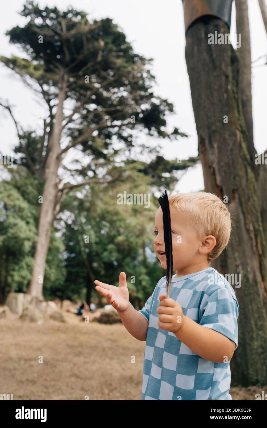 Kaukasischer Kleinkind mit schwarzer Krähenfeder, die im Park gefunden wurde Stockfoto