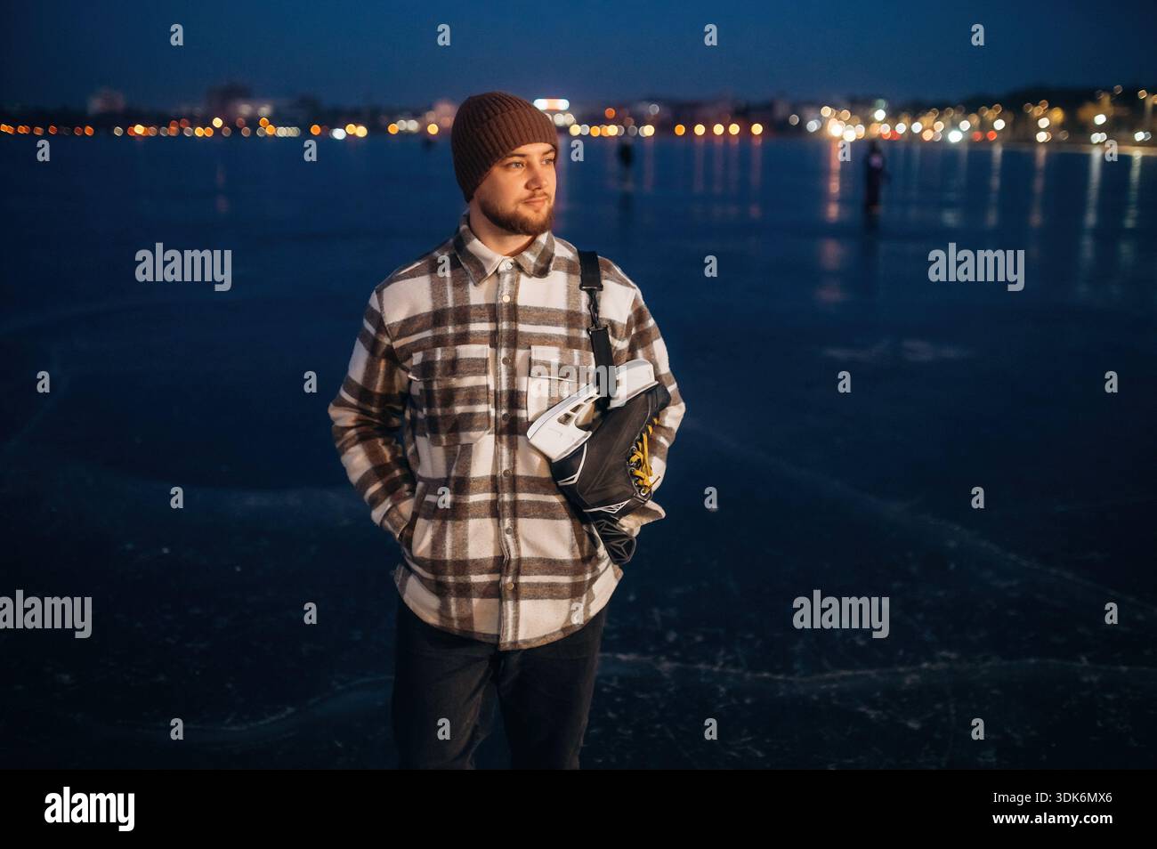 Stehen und weit weg schauen. Ein Mann ist im Winter mit seinen Schlittschuhen auf dem Eis. Stockfoto
