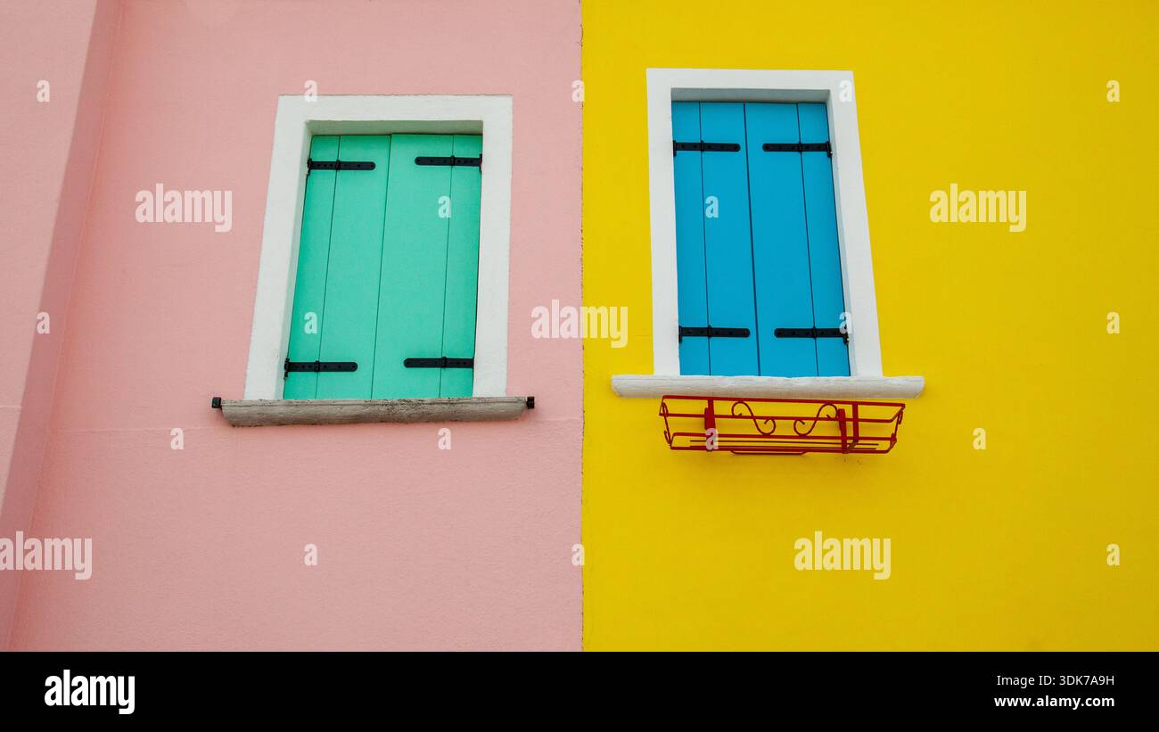 Zwei Fenster mit grünen und blauen Fensterläden an rosa und gelben Wänden, nebeneinander Stockfoto