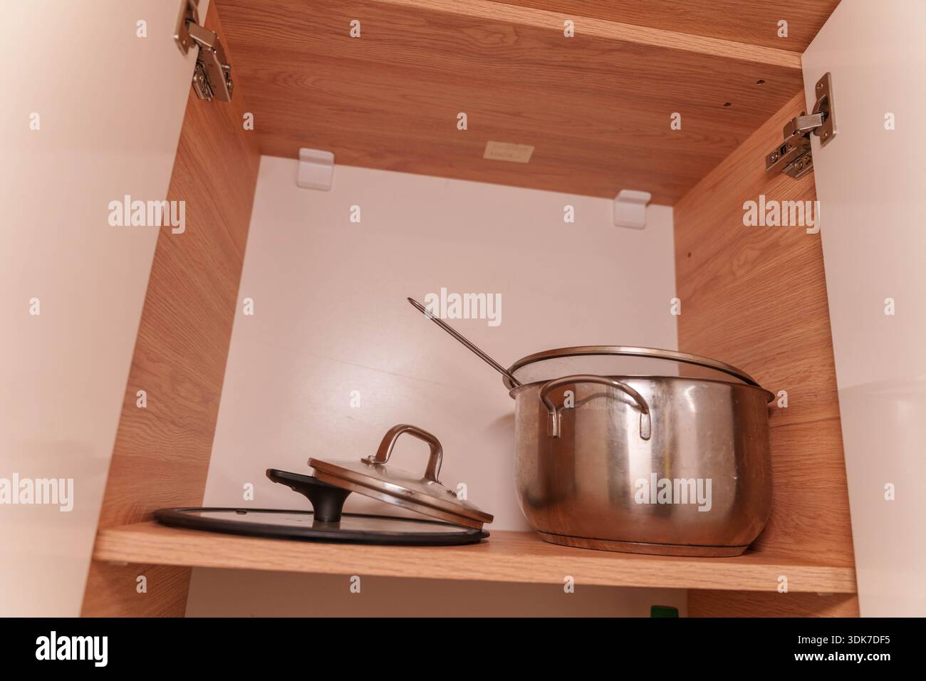 Offener Küchenschrank mit Töpfen, Tellern, Tassen und Utensilien auf Holzregalen Stockfoto