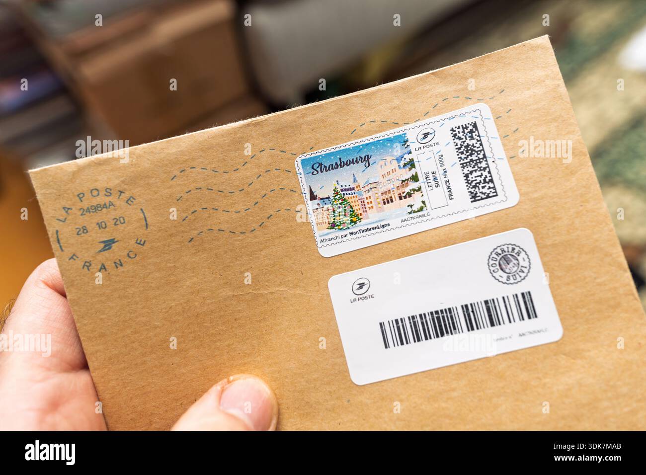 Elsass, Frankreich - 23. März 2024: Nahaufnahme einer Hand, die einen braunen Umschlag mit Straßburger Briefmarke und Tracking-Etikett für Postdienst hält Stockfoto