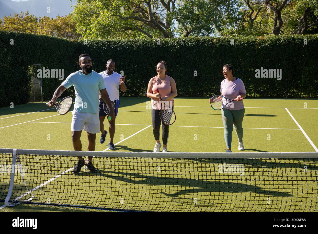 Verschiedene Freunde in Sportbekleidung gehen gemeinsam auf dem Rasenplatz mit Tennisschlägern in der Nähe des Netzes. Athletik, Kameradschaft, Freizeit, Outdoor, Lifestyle, kraftvoll, Harmonie || Modell veröffentlicht Stockfoto