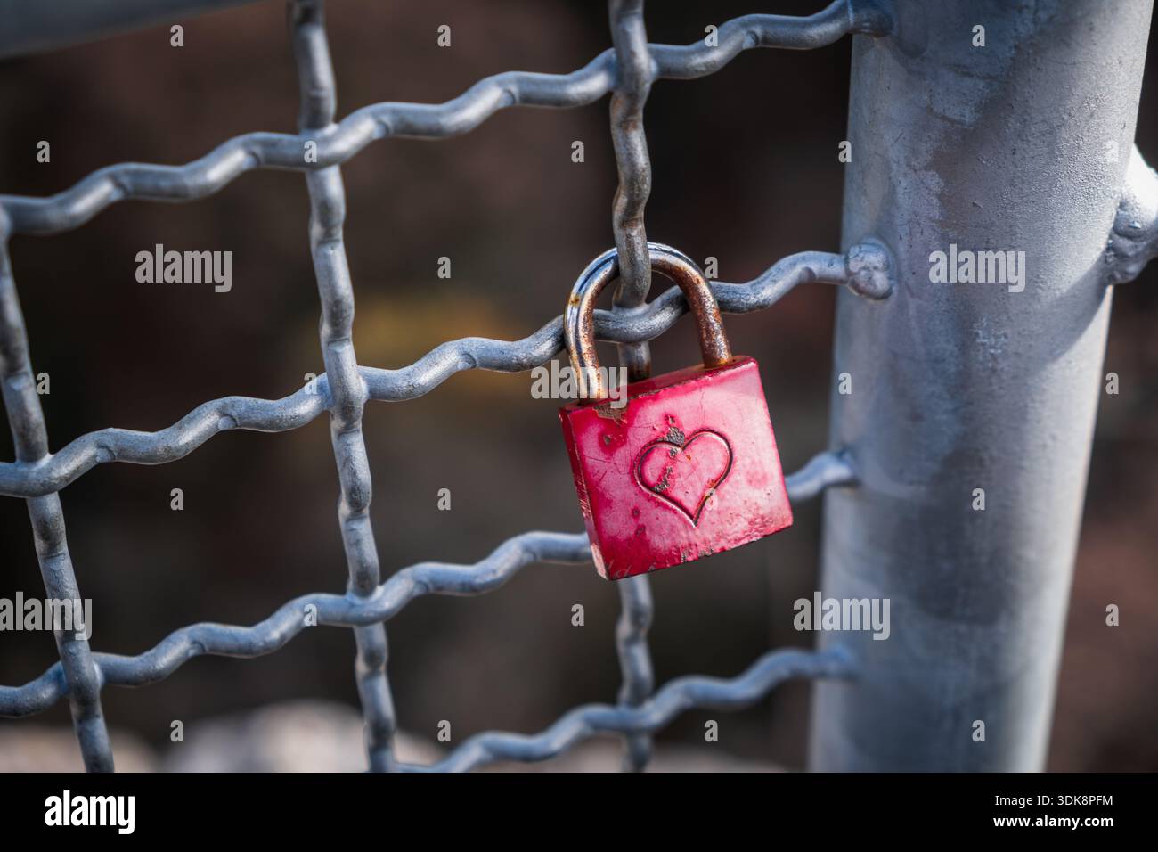 Rostrotes Vorhängeschloss mit Herz auf Geländer, symbolisiert einsame, unerwiderte Liebe, Herzschmerz, Verlassenheit, emotionalen Schmerz, Beziehungskonzept. Stockfoto