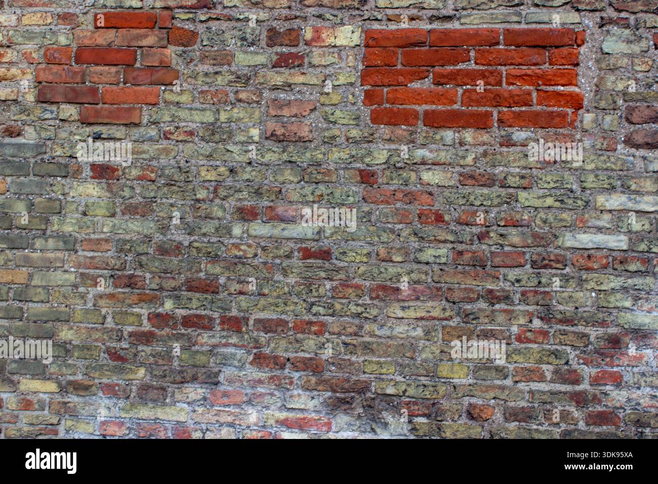 Verwitterte alte Ziegelmauerstruktur mit gemischten roten und gelben Ziegeln und sichtbaren Mörtelmustern. Städtischer architektonischer Hintergrund mit veraltetem Mauerwerk Stockfoto