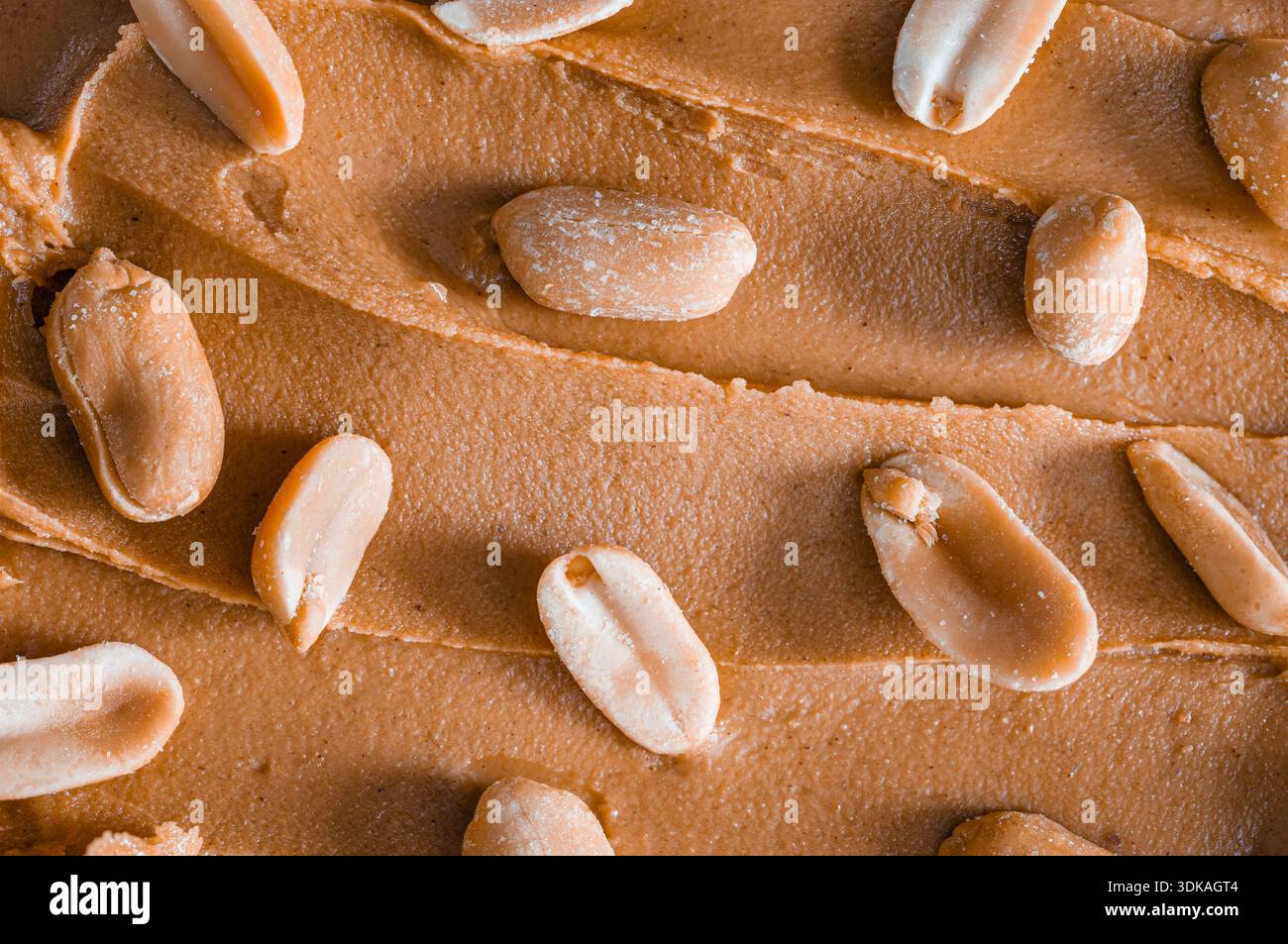 Erdnüsse mit Schale, verstreut auf einem Hintergrund aus cremiger Erdnussbutter Stockfoto
