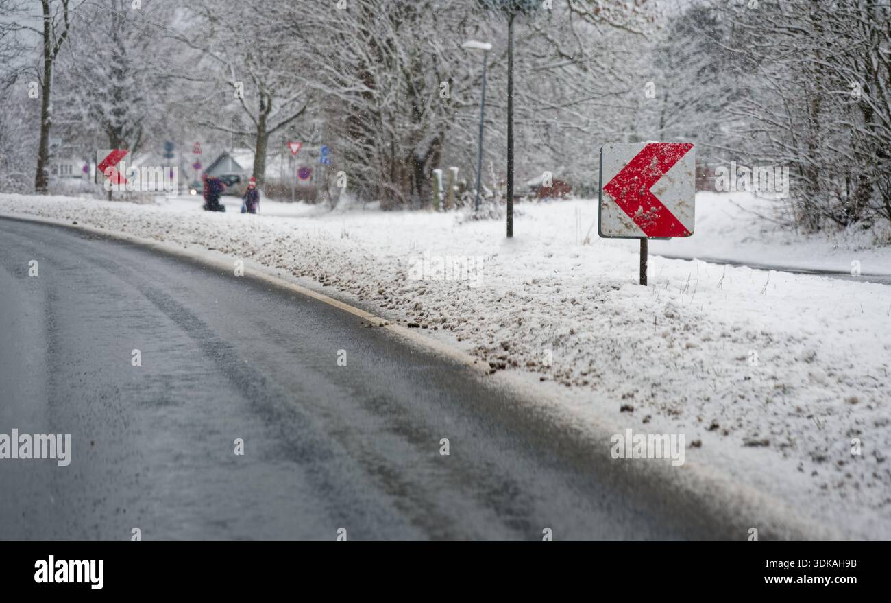Rote und weiße Chevron-Warnschilder auf einer rutschigen kurvenreichen Straße, die mit Schnee bedeckt ist. Gefährliche Fahrbedingungen während eines schweren Schneesturms. Stockfoto