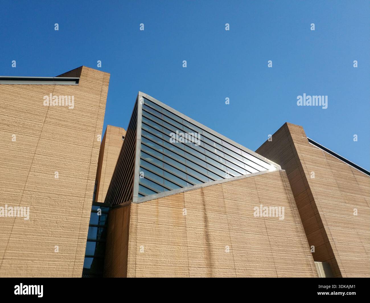 Flachwinkelansicht komplexer moderner Architekturstrukturen mit scharfen Winkeln, beigefarbenen Steinstrukturen und Glaselementen. Stockfoto