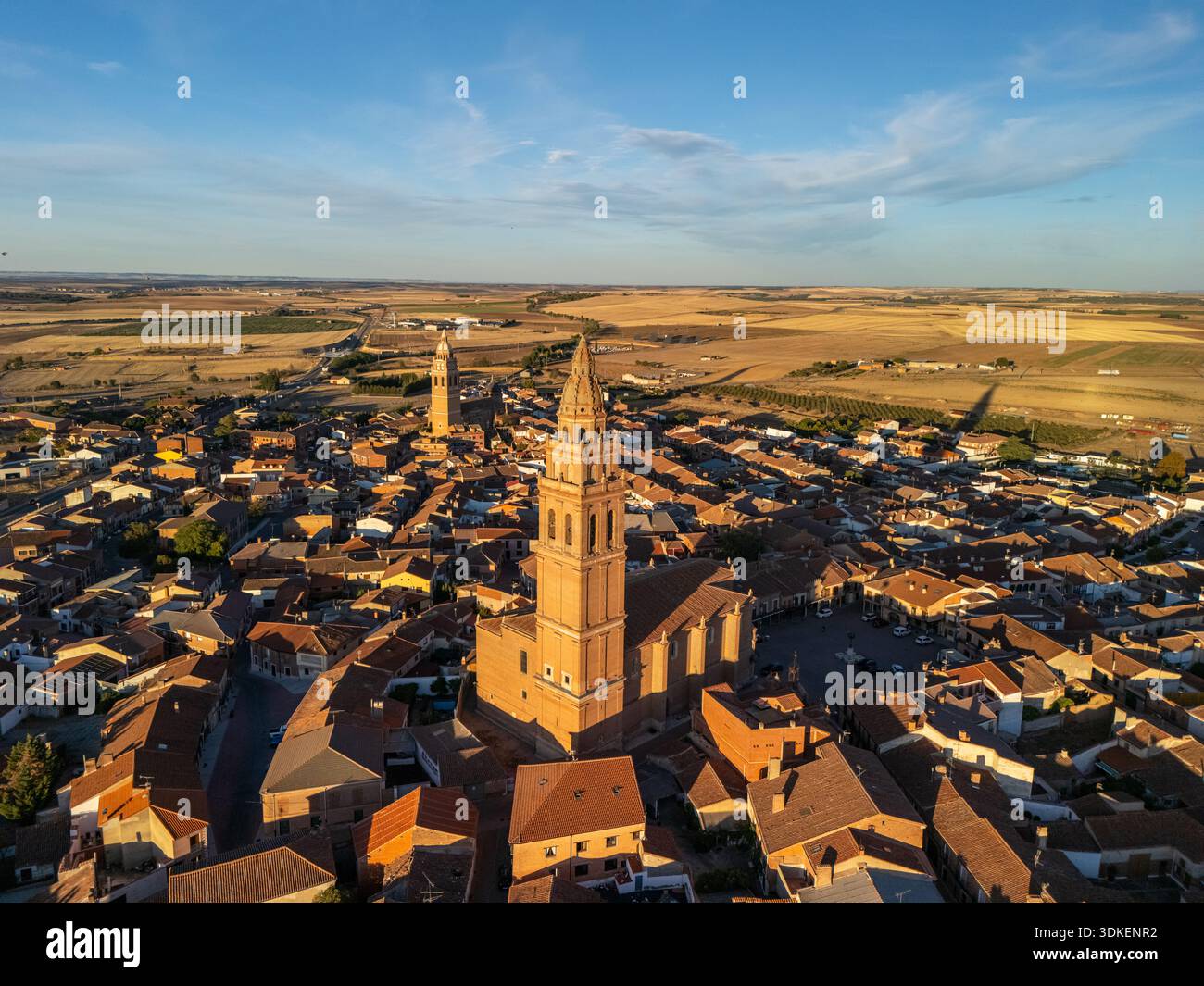 Luftaufnahme einer malerischen europäischen Stadt mit roten Ziegeldächern, zwei hohen Kirchtürmen und einer weiten Landschaft, die bei Sonnenuntergang leuchtet: Alaejos, Castile und Leon Stockfoto