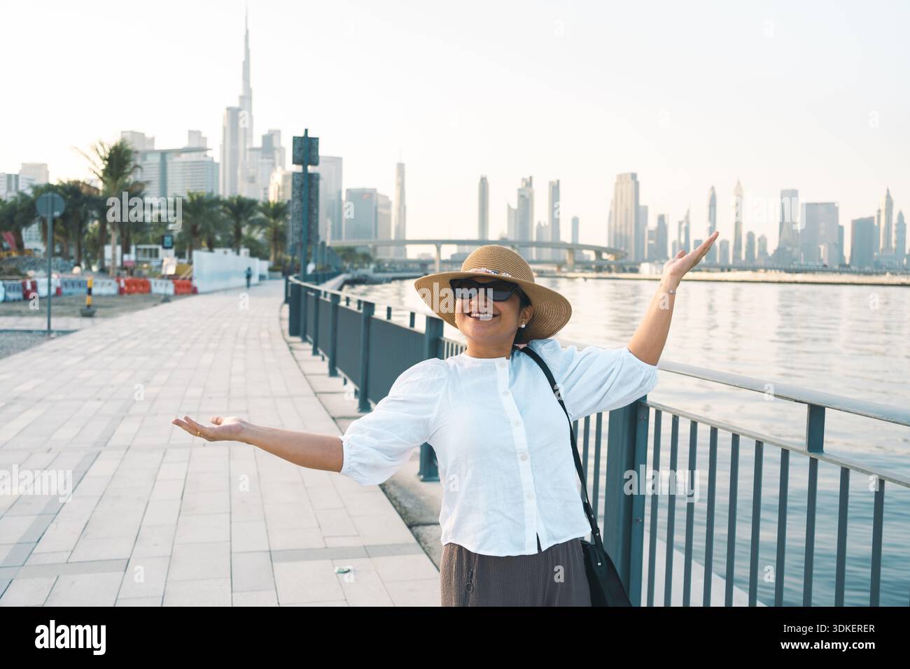 Glückliche Frau posiert am Ufer von Dubai mit modernem Skyline-Hintergrund Stockfoto
