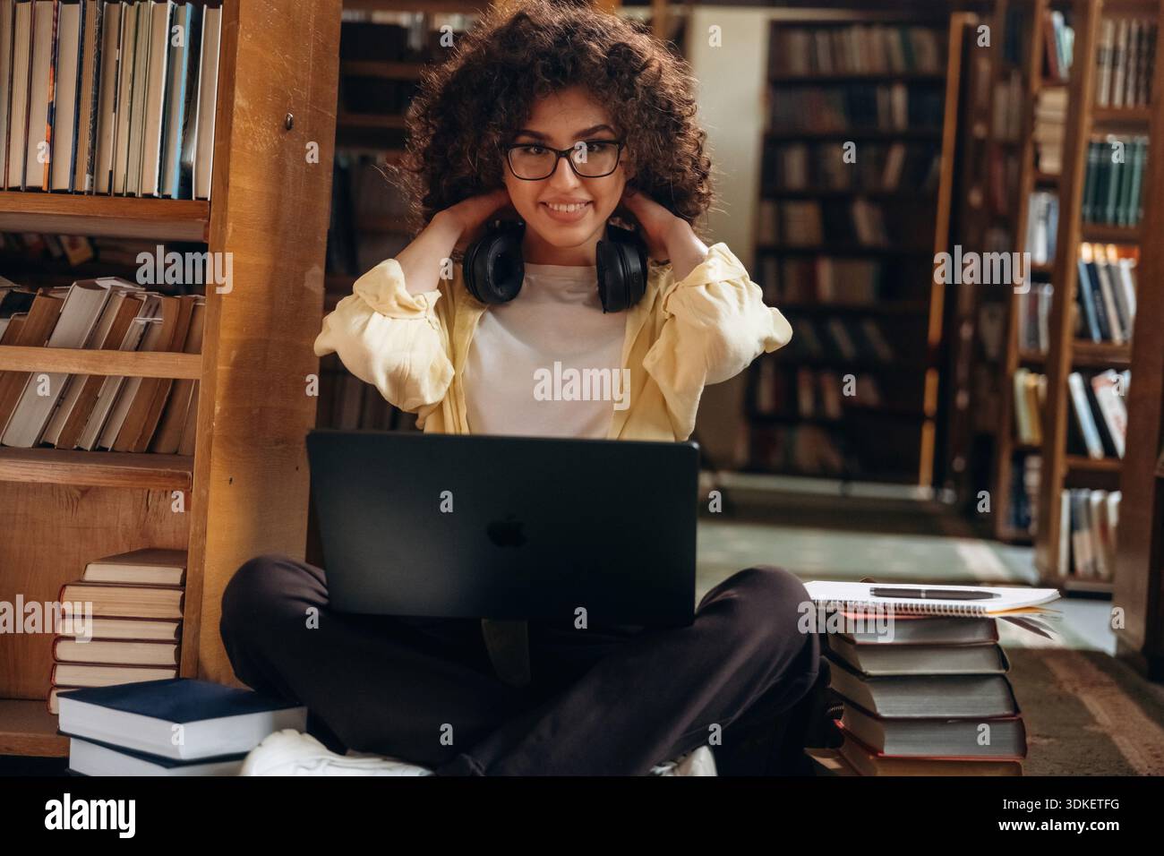 Der Laptop liegt auf den Beinen. Die schöne Frau ist in der Bibliothek. Stockfoto
