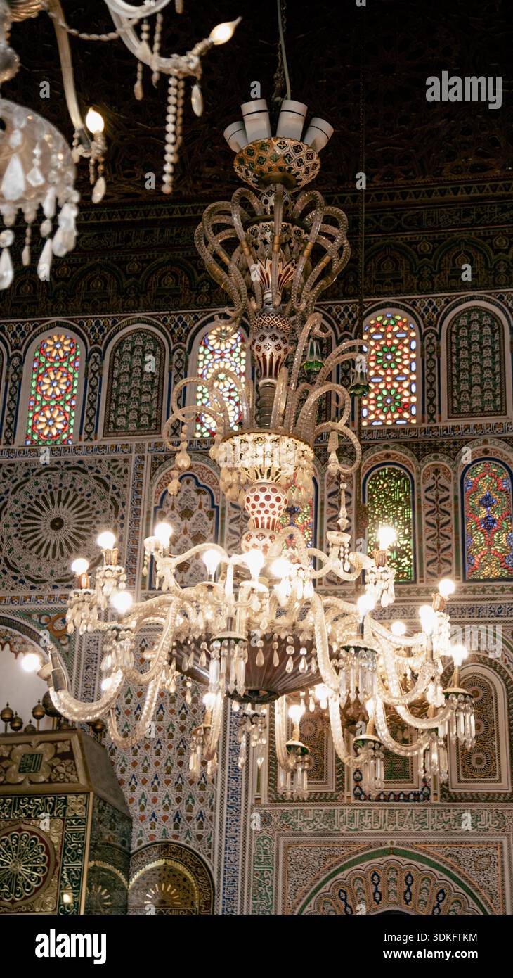 Monumentales Glas und Kristallleuchter in einer Fès-Madrasa, umgeben von zellige Fliesen, geschnitztem Stuck und fein farbigen traditionellen marokkanischen Färbungen Stockfoto