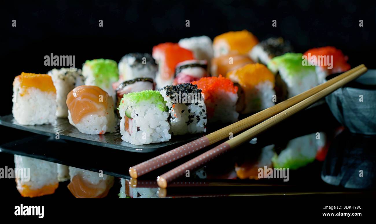 Kollektion Von Farbenfrohen Sushi, Die Kunstvoll Auf Glänzendem Dunklem Sockel Positioniert Sind, Mit Weicher Beleuchtung Für Atmosphäre Stockfoto