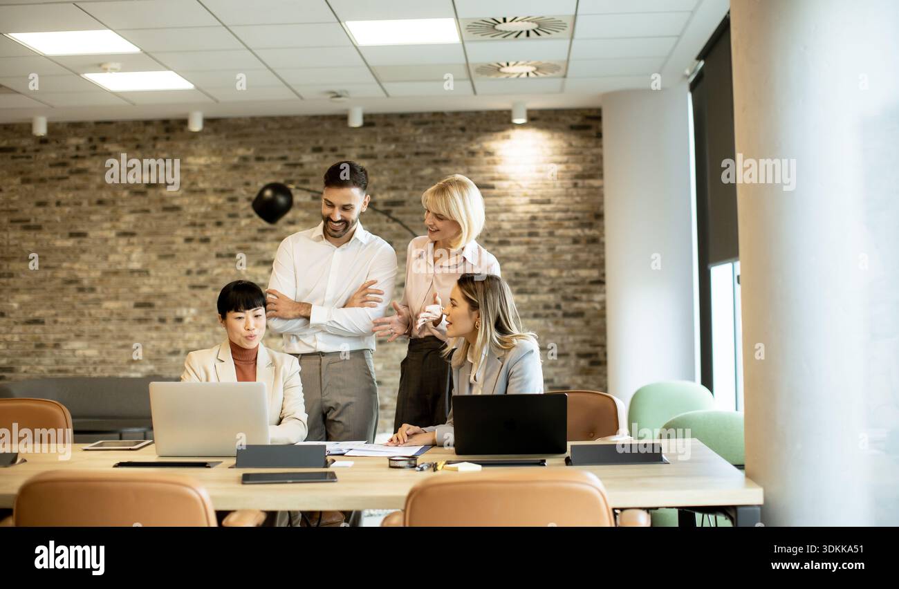 Eine Gruppe von vier Fachleuten nimmt an einem Tisch in einem hellen, modernen Büro Teil. Sie besprechen Projektdetails, während sie Inhalte auf prüfen Stockfoto