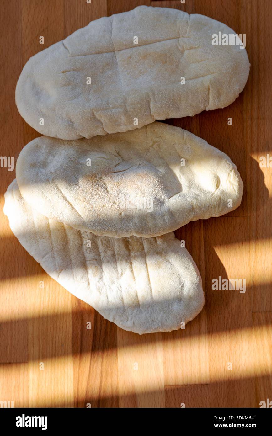 3 hausgemachte weiße Pitta-Brote auf einem hölzernen Schneidebrett mit Schatten Stockfoto