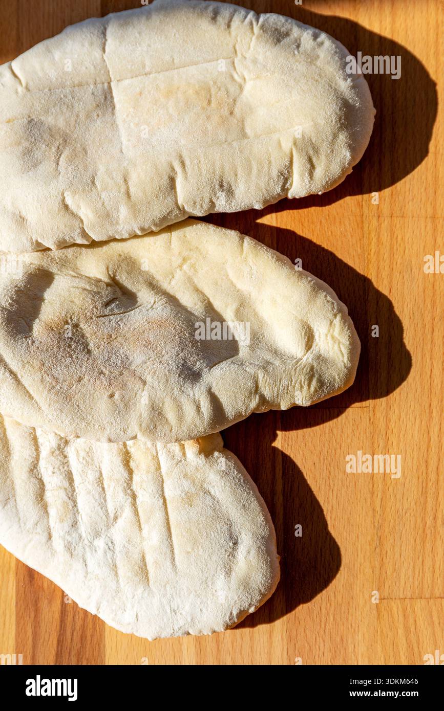 3 hausgemachte weiße Pitta-Brote auf einem hölzernen Schneidebrett mit Schatten Stockfoto