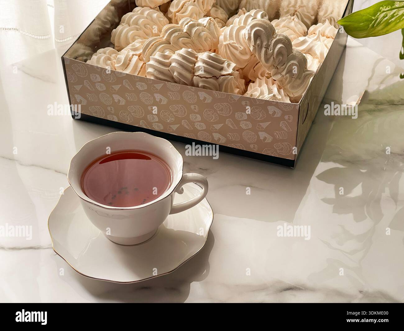 Tee mit Zephyr Marshmallows. Gemütliche Teezeit mit einer Tasse heißem schwarzem Tee und weichen, luftigen russischen zephyr Marshmallows auf einem Leuchttisch in der Nähe des Fensters. Stockfoto