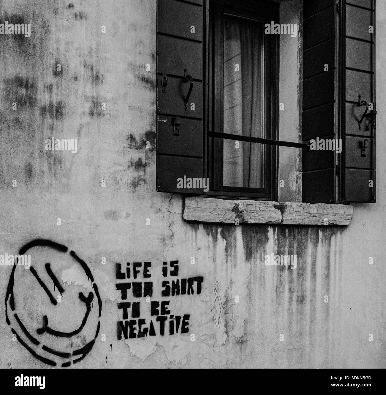 Venedig, Italien. Februar 2026. Graffiti mit der Aufschrift „das Leben ist zu kurz, um negativ zu sein“ erscheinen an einer verwitterten Wand unter einem Fenster in Venedig Stockfoto