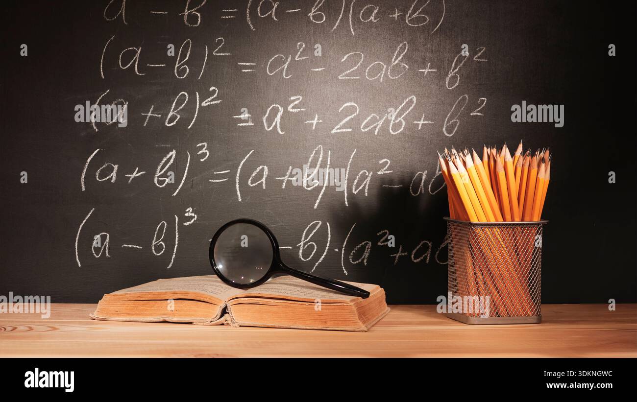 Zurück zur Schule, Bleistiftkorb, Lehrbuch, Lupe auf dem Tisch vor schwarzer Tafel mit algebraischen mathematischen Formeln, geschrieben mit weißem Cha Stockfoto