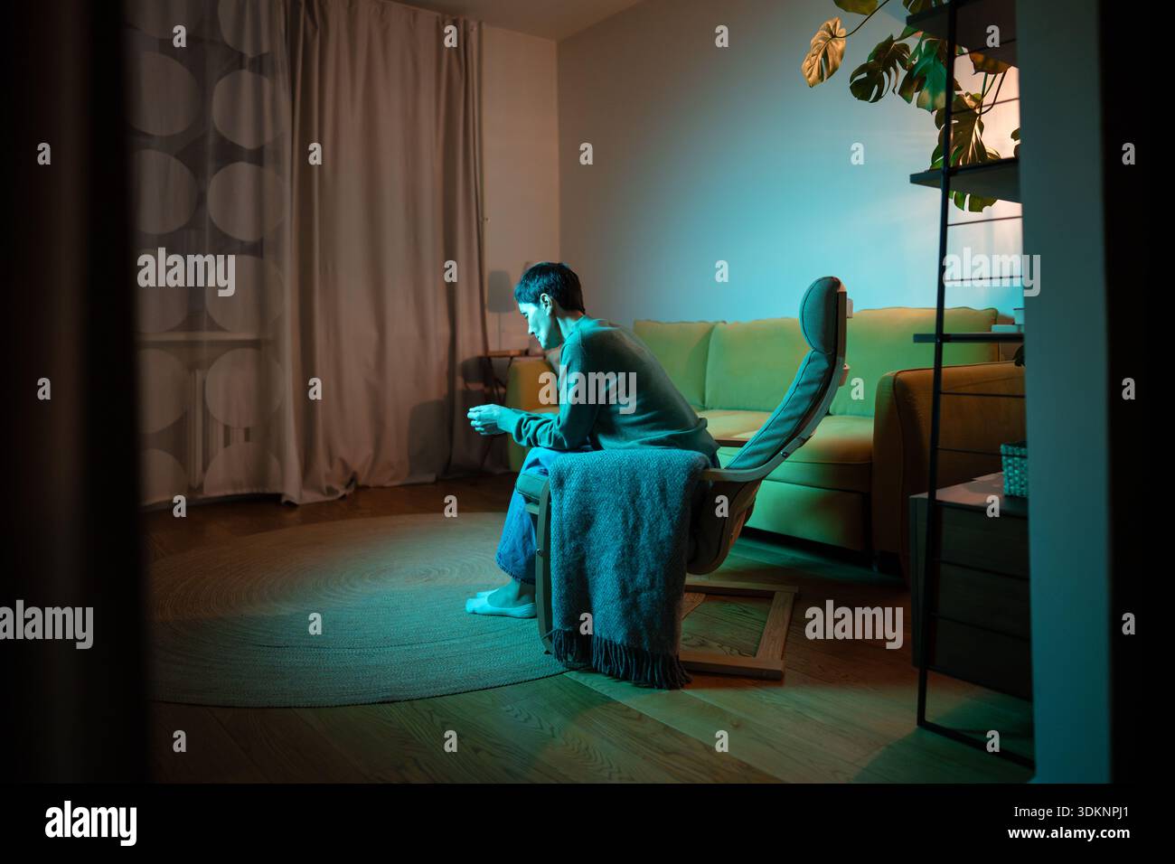 Verärgerte Seniorin mit verlorenem Ausdruck, die allein im Wohnzimmer sitzt und sich mit persönlichem Drama beschäftigt. Stockfoto