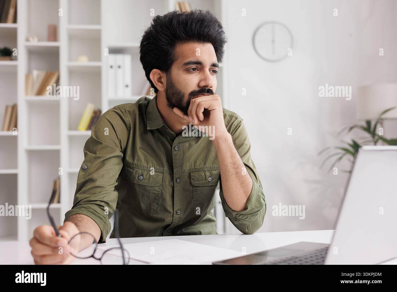 Der müde Indianer nimmt die Brille ab, leidet unter schmerzhaften Empfindungen, hat Probleme mit Astigmatismus. Ein Mann, der nach einem langen Arbeitstag auf der Komm gestresst hat Stockfoto