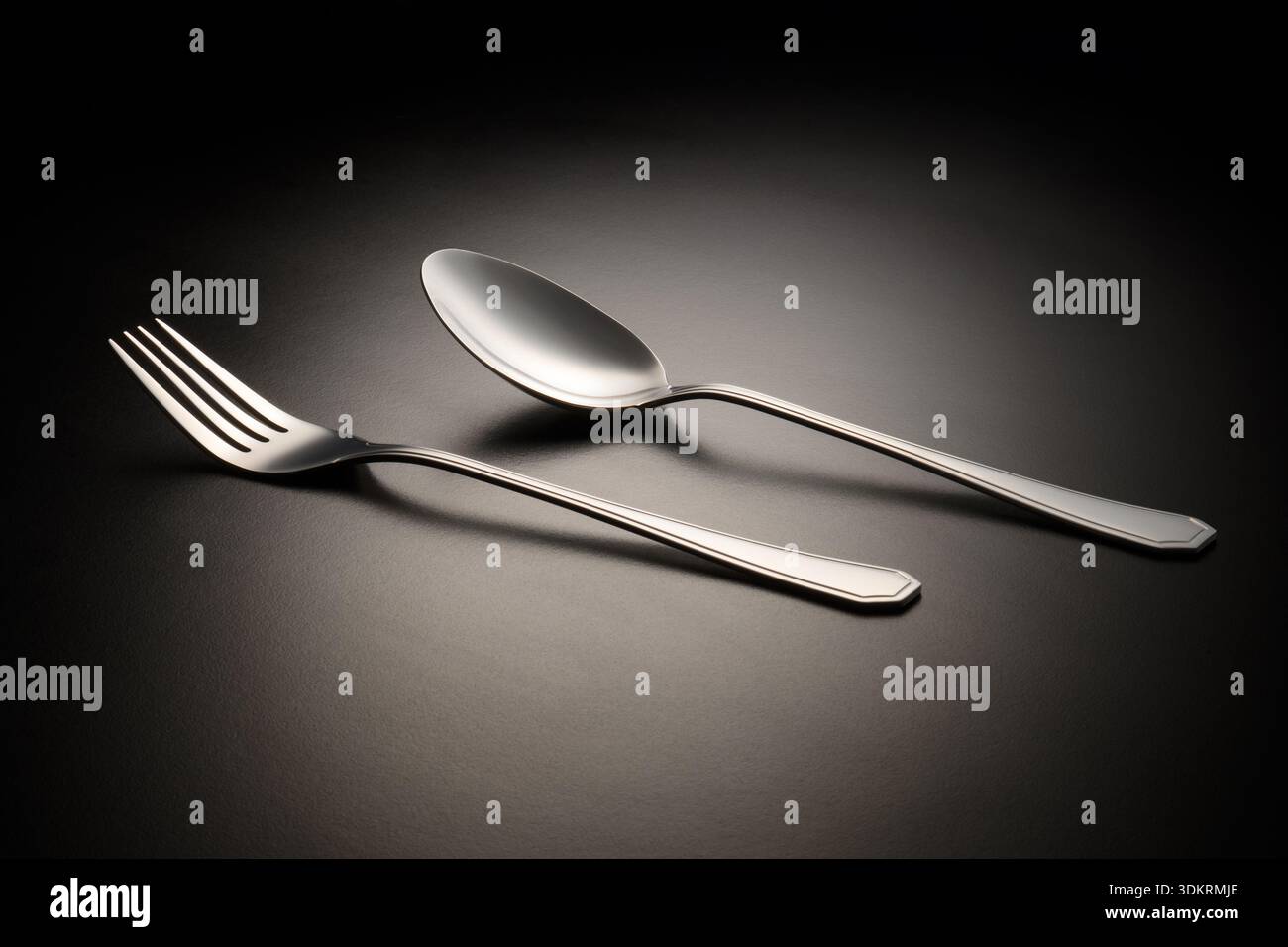 Modernes Besteckset aus Edelstahl mit Gabel und Löffel mit klaren Linien und minimalistischem Design, fotografiert auf einer dunklen Oberfläche mit Farbverlauf. Stockfoto