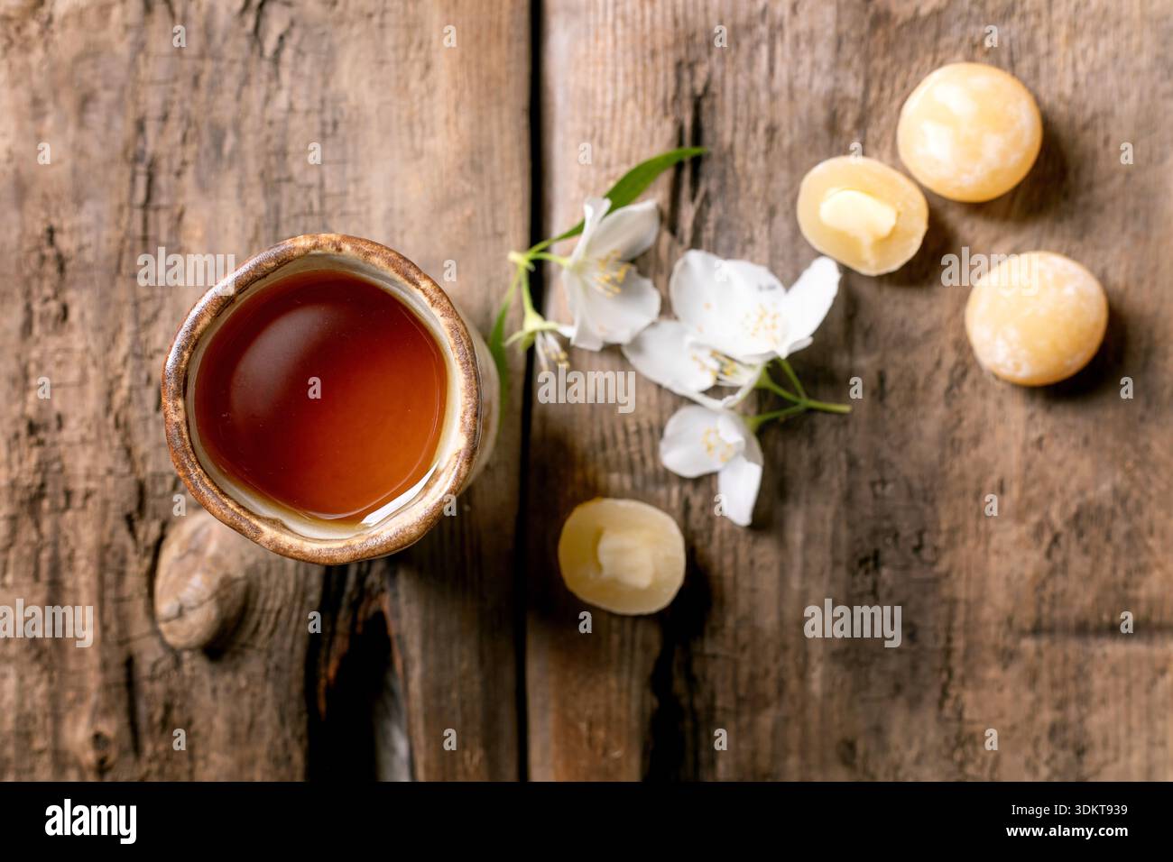 Keramik-Teetasse auf rustikalem Holztisch, dekoriert mit weißen Jasminblüten und traditionellen asiatischen Süßigkeiten Mochi-Kugeln von oben Stockfoto