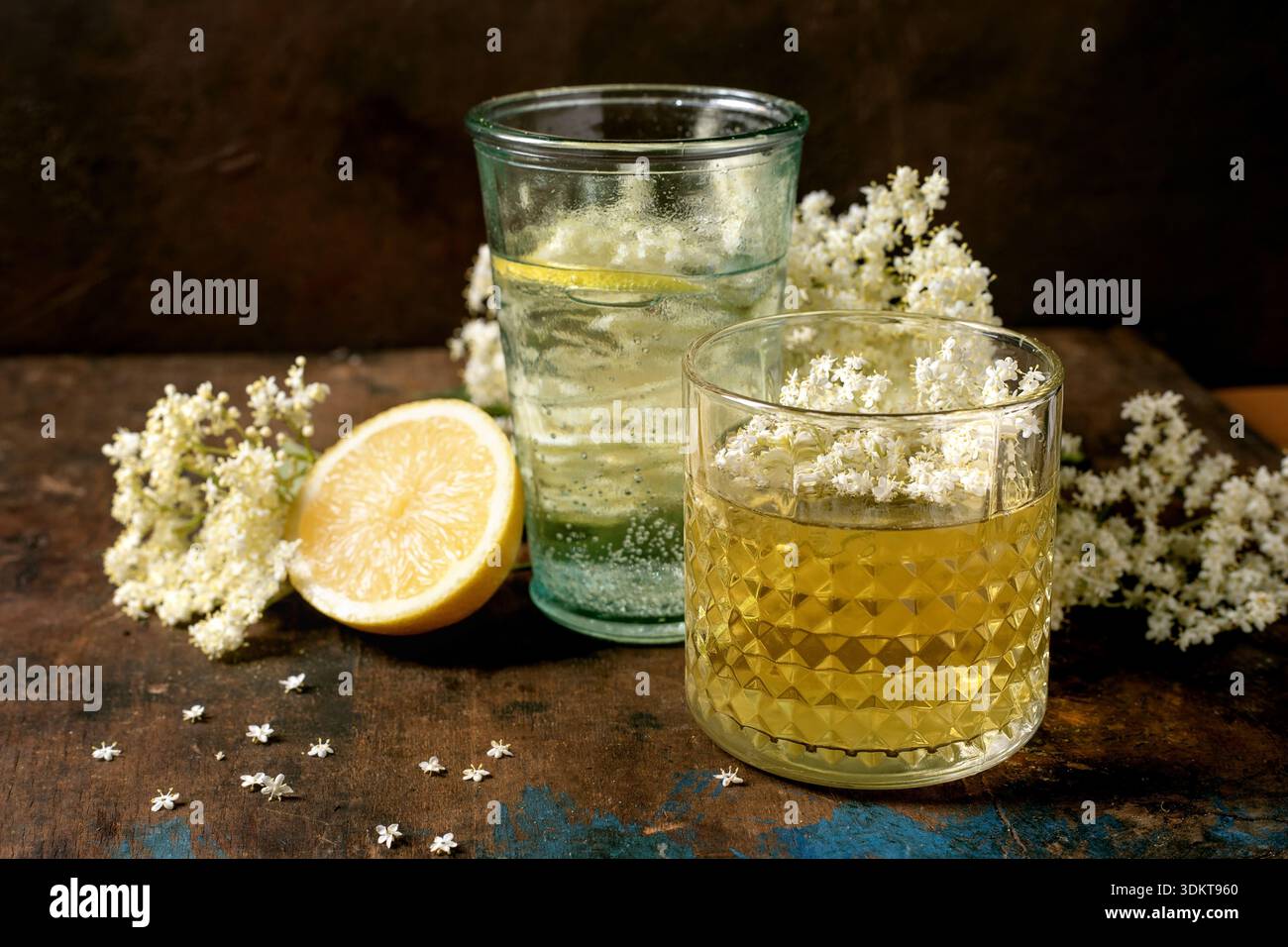 Zwei Gläser Holunderblütenkordial mit weißen Holunderblüten und Zitronenscheibe auf rustikalem Holztisch Stockfoto