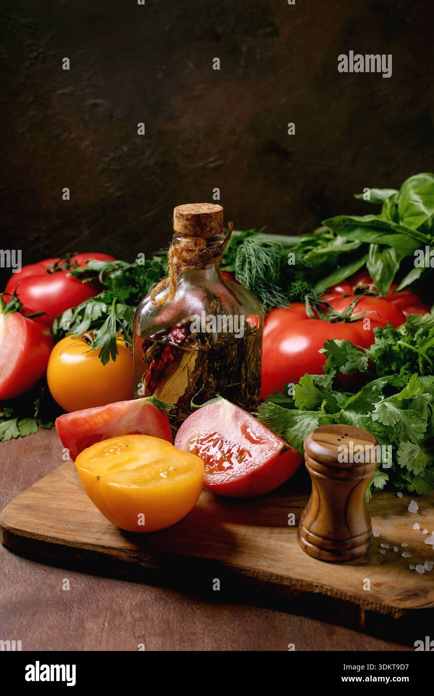 Frische Tomaten Kräuter Olivenölflasche auf hölzernem Schneidebrett. Gesunde Kochzutaten mit Salz Pfeffermühle Basilikumblätter Stockfoto