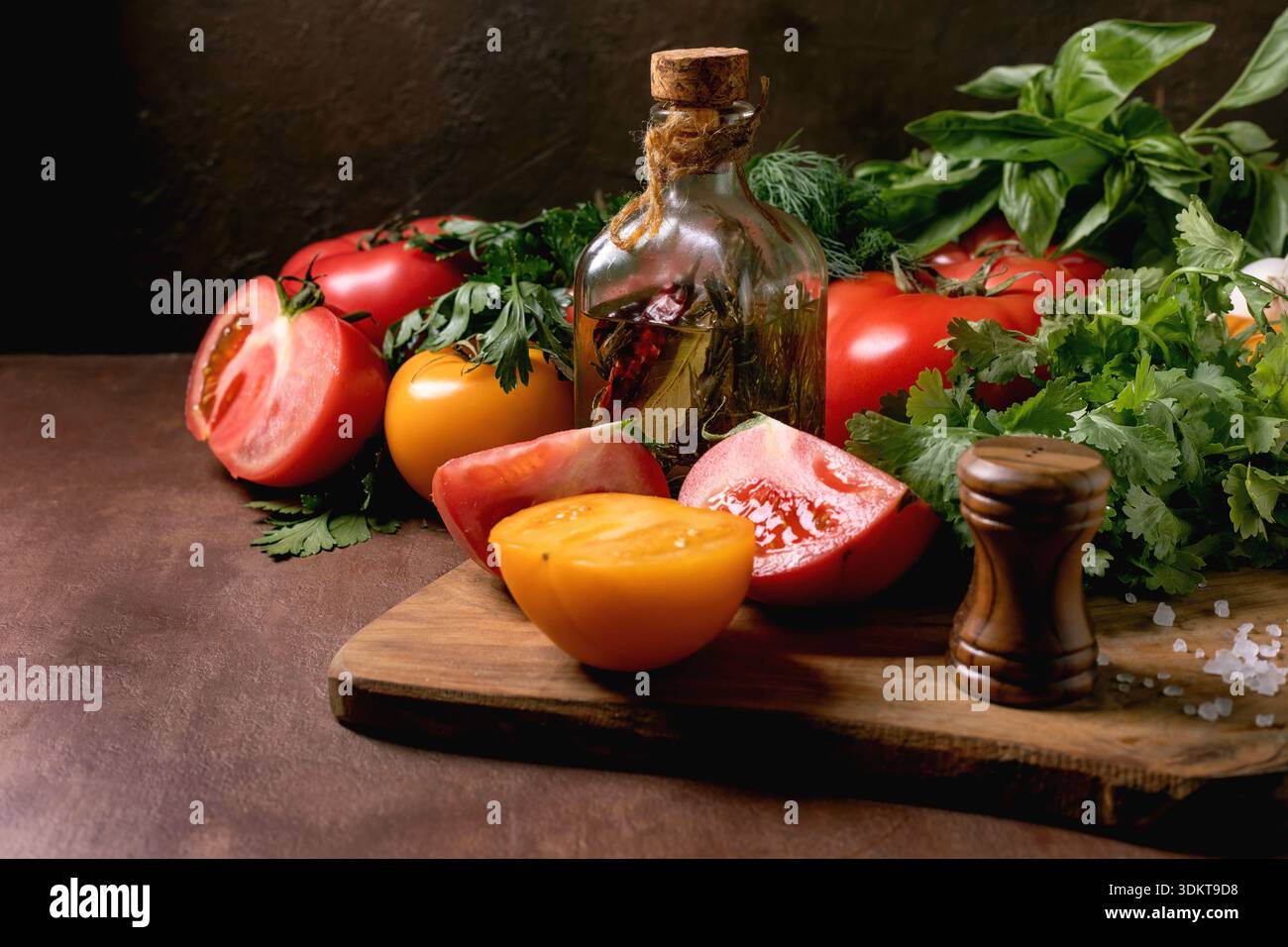 Frische rote gelbe Tomaten Kräuter Olivenöl Flasche Salz Pfeffermühle auf hölzernem Schneidebrett. Gesundes Kochen Zutaten Küchenzubereitung Konzept. Stockfoto