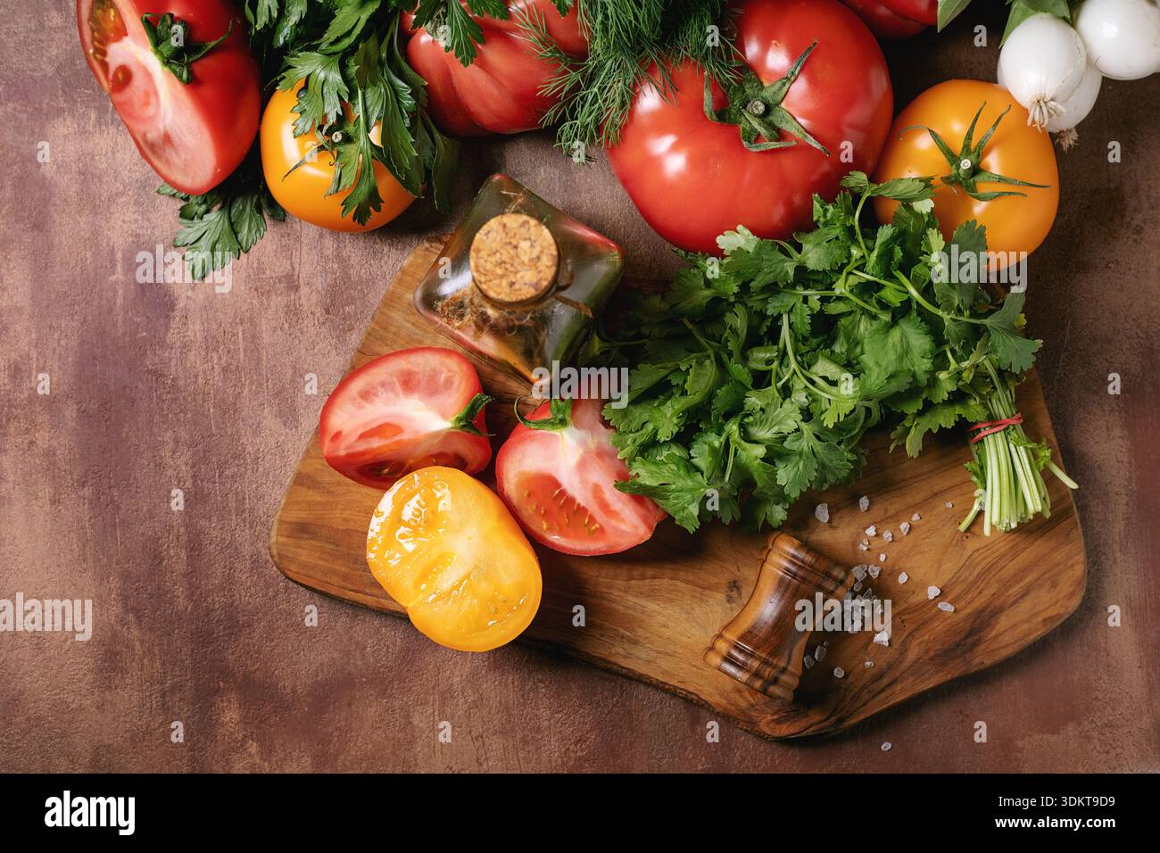 Frische Tomaten Paprika Kräuter Knoblauch auf hölzernem Schneidebrett mit Salz Pfeffermühle angeordnet. Bunte Gemüse-Kochzutaten Stockfoto