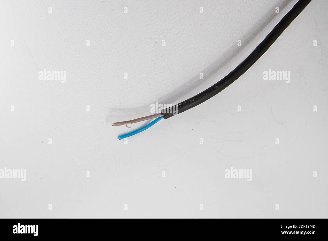 Freiliegendes elektrisches Kabel mit abisolierter Isolierung und sichtbaren Drähten auf weißem Hintergrund Stockfoto