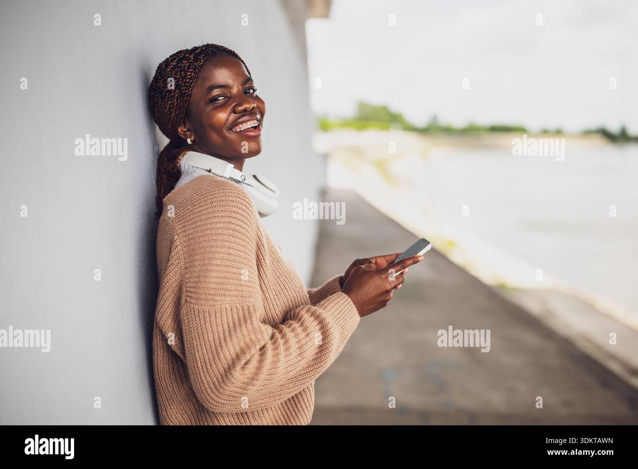 Außenporträt einer glücklichen jungen schwarzen Frau, die Nachrichten auf dem Smartphone sendet. Stockfoto